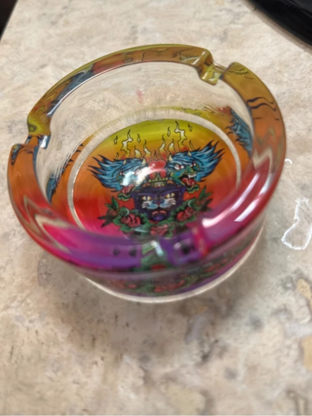 A round iridescent glass ashtray with a tattoo-style feline graphic.